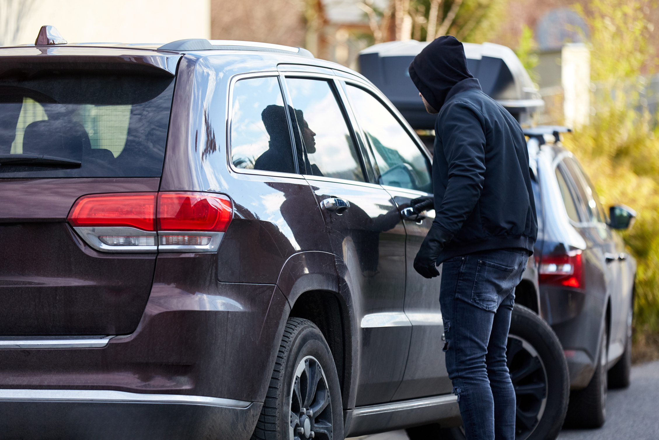 Thief peering into lear untinted windows of Jeep Cherokee SUV, looking for items to steal that have been left out on the passenger seat or floorboards. 