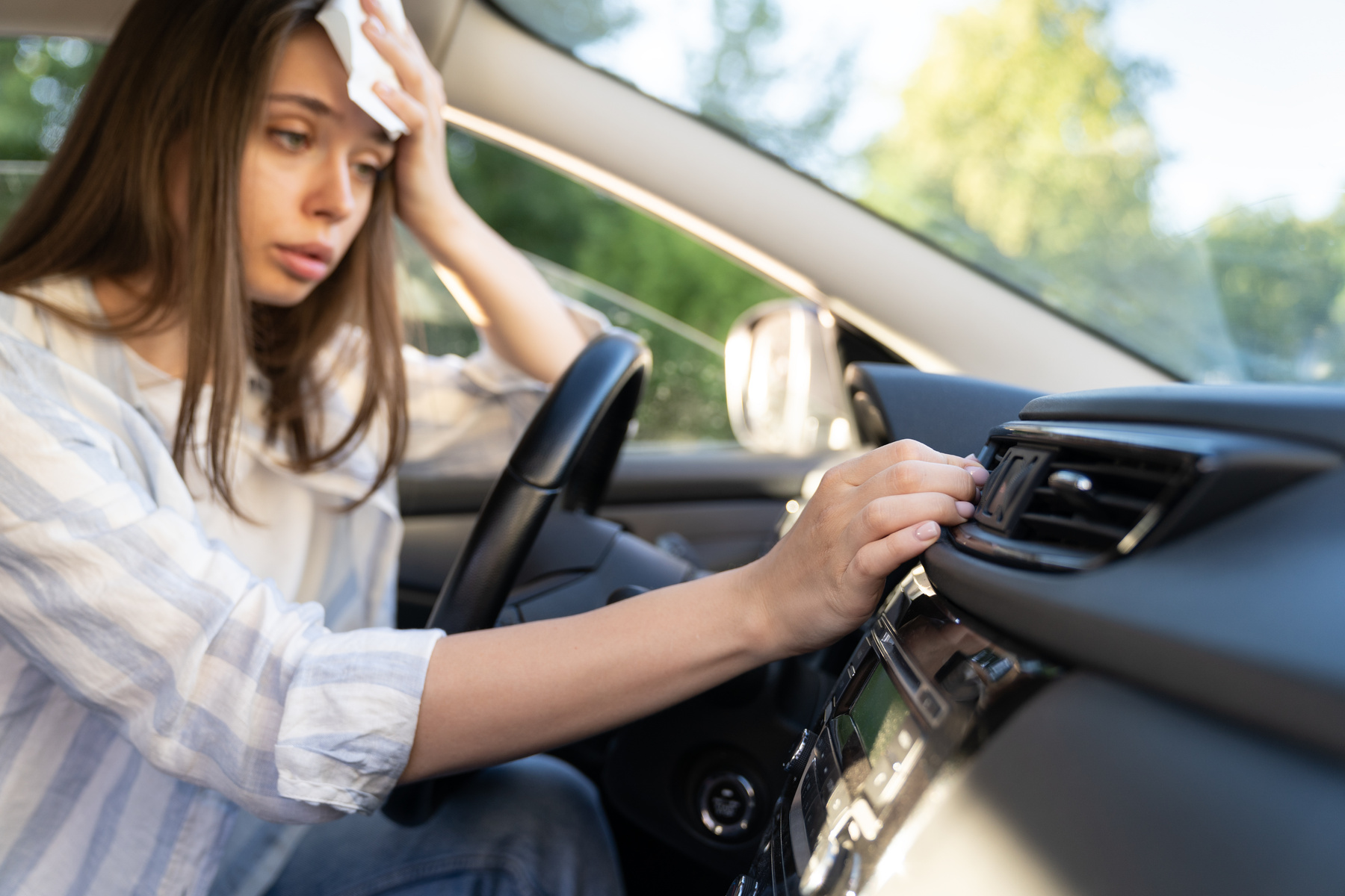 Woman in her untinted car sweating due to excessive heat from high summer temperatures.